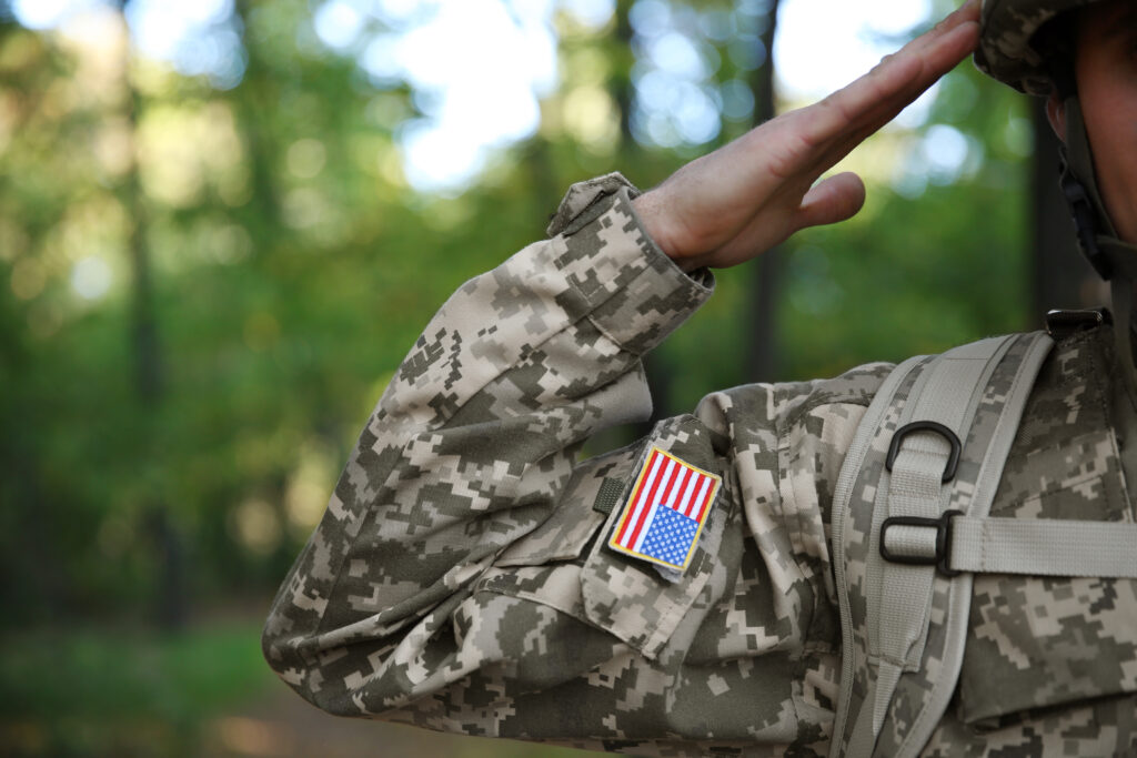 person in military uniform with US flag on sleeve saluting