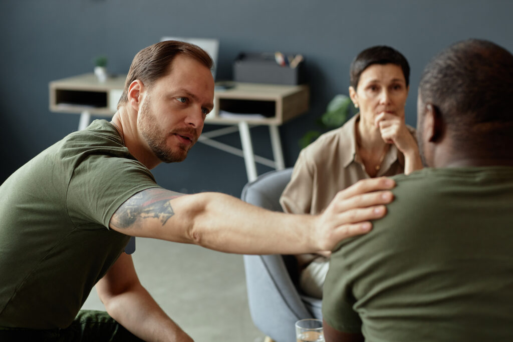 man with hand on another man's shoulder and woman listenting